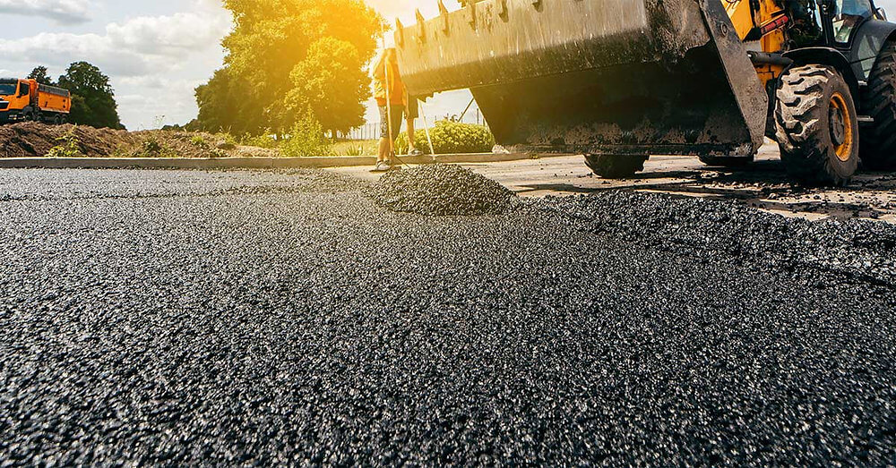 Heavy machinery paving a new asphalt road at sunset