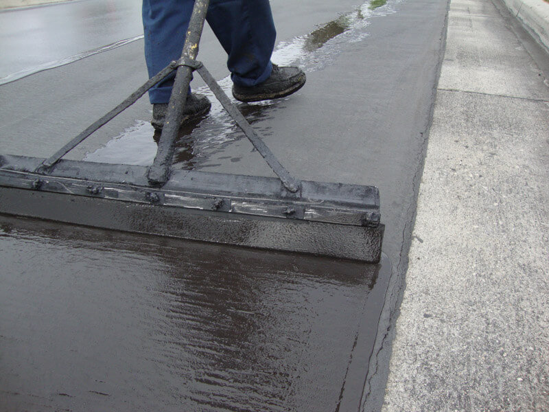 A machine applying a fresh layer of sealcoat to an existing asphalt parking lot.